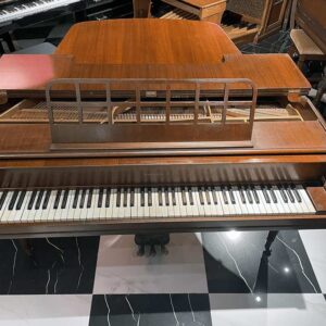 Vintage wooden upright piano with keyboard exposed on a black-and-white checkered floor, showing its old-fashioned aesthetic.